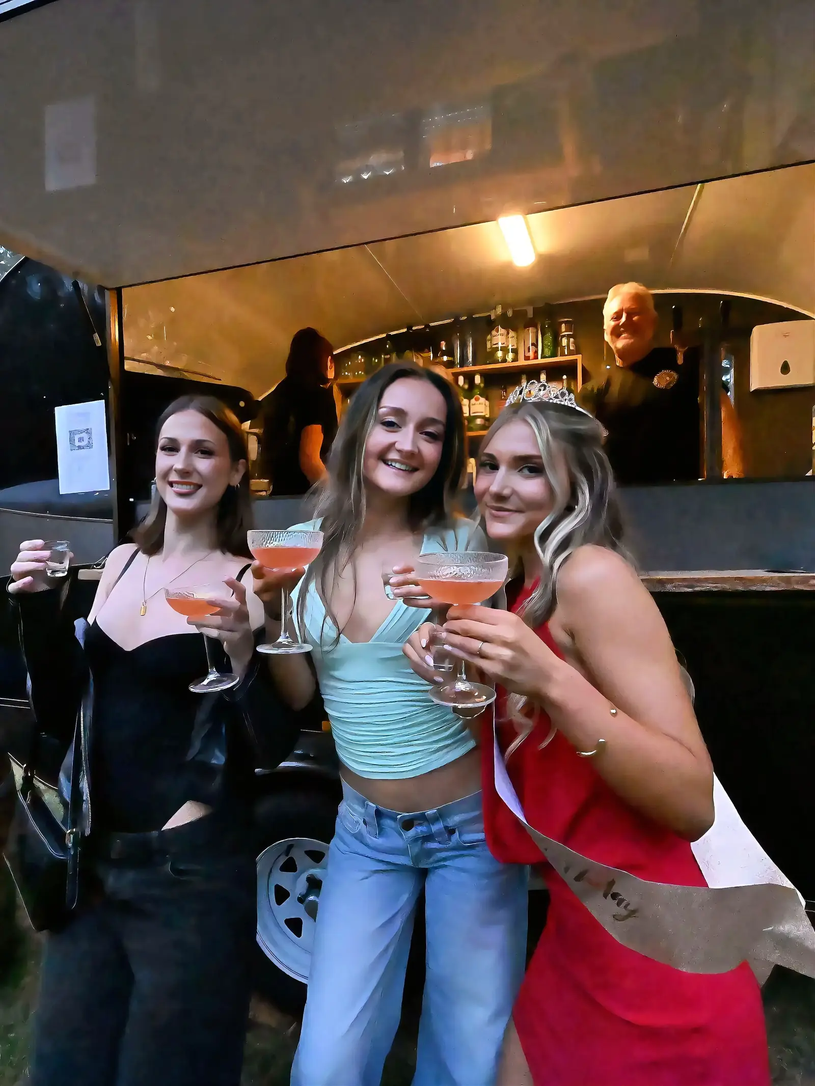 Birthday girl in a tiara and sash with friends holding cocktails at the mobile bar van at her 18th birthday party